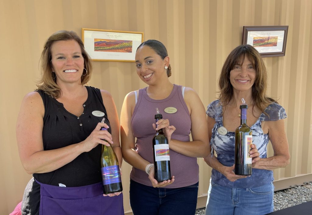 A photograph showing three Darcie Kent Estate Winery employees, each holding a bottle of wine.